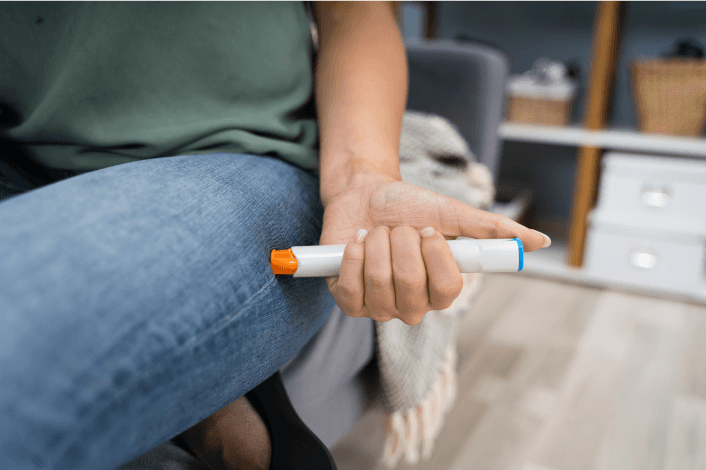 Person holding an injection pen in their hand while sitting.