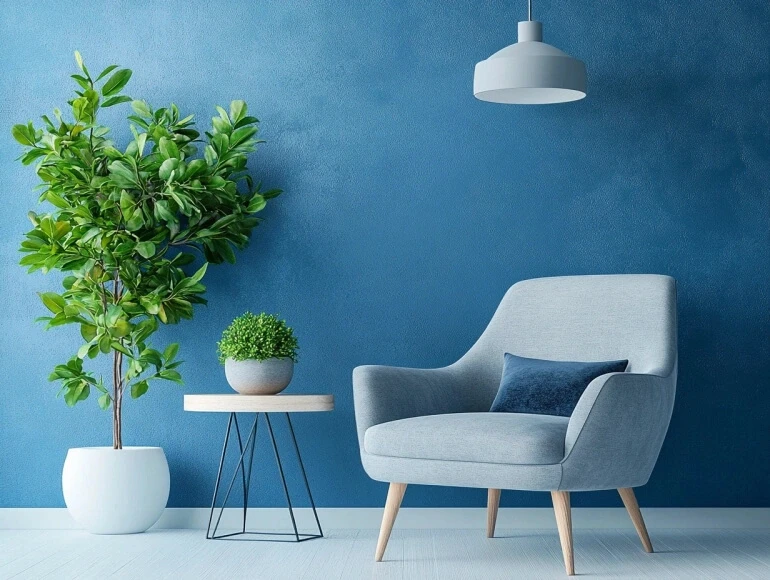 Modern living space with a light gray armchair, blue accent pillow, potted plants, and a round side table against a blue t