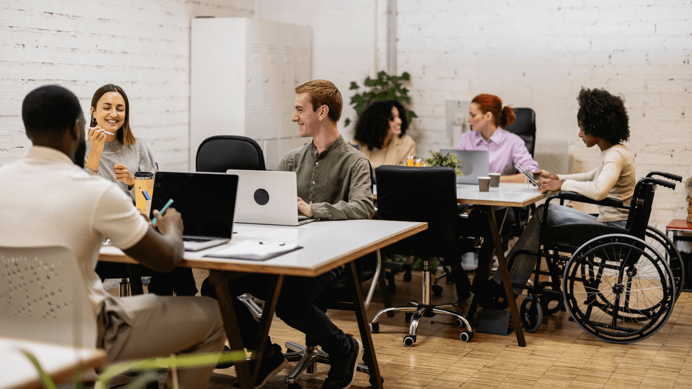 A diverse group of employees people engaged in a meeting around a conference tables, one in a wheelchair.