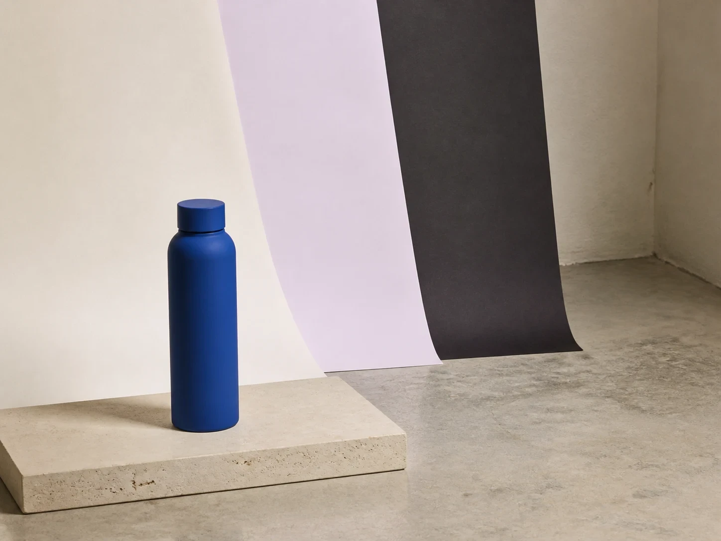 Unbranded cobalt bottle on limestone with three restrained physical backdrop treatments
