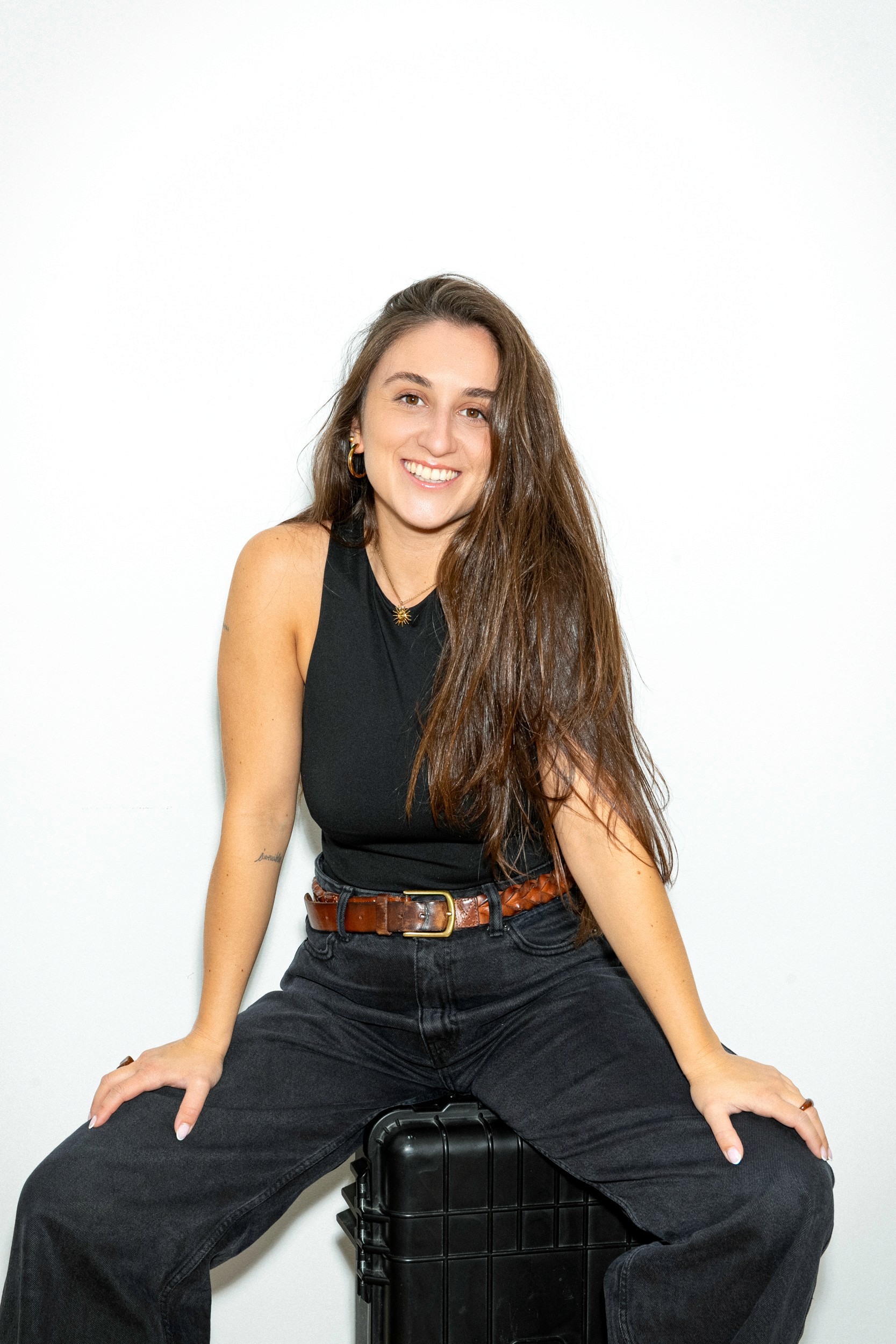 Professional portrait of a woman with wavy brown hair, wearing a black blazer and beige top, smiling warmly against a light background.
