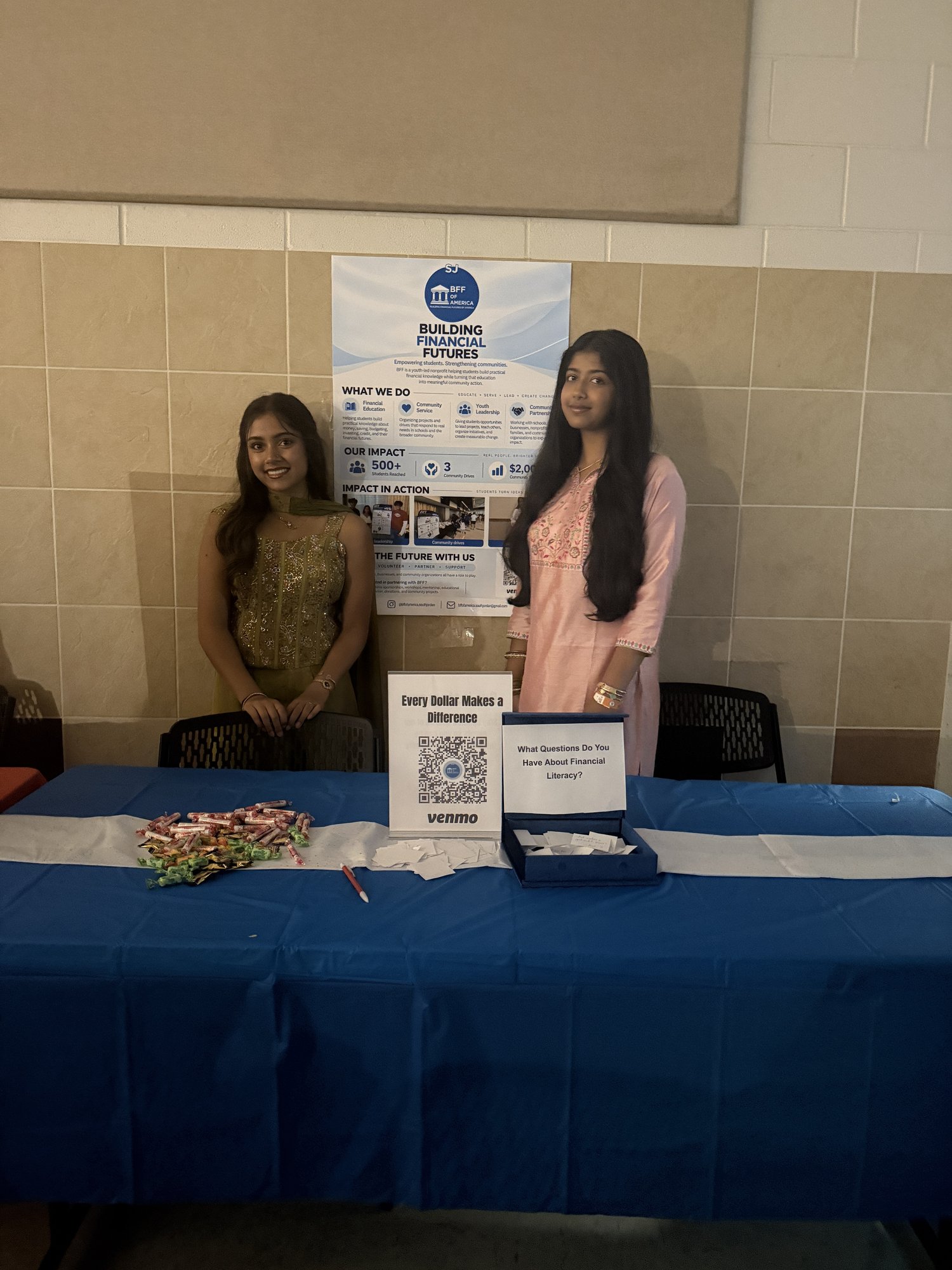 Two BFF volunteers stand behind an outreach table with a BFF poster and question box.