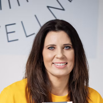 Woman with dark hair smiling, wearing yellow shirt.