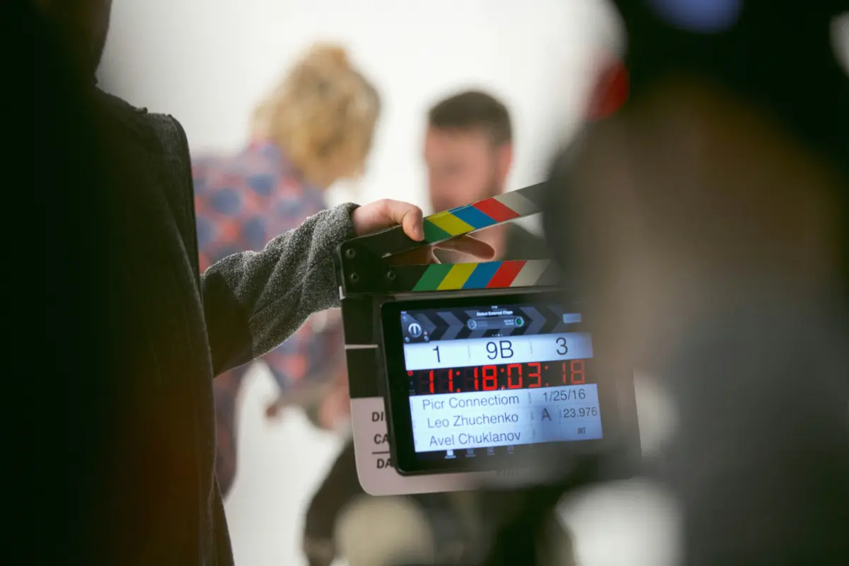 Filmton, ein Set einer Filmaufnahme mit einer Filmklappe und Schauspielern im Hintergrund