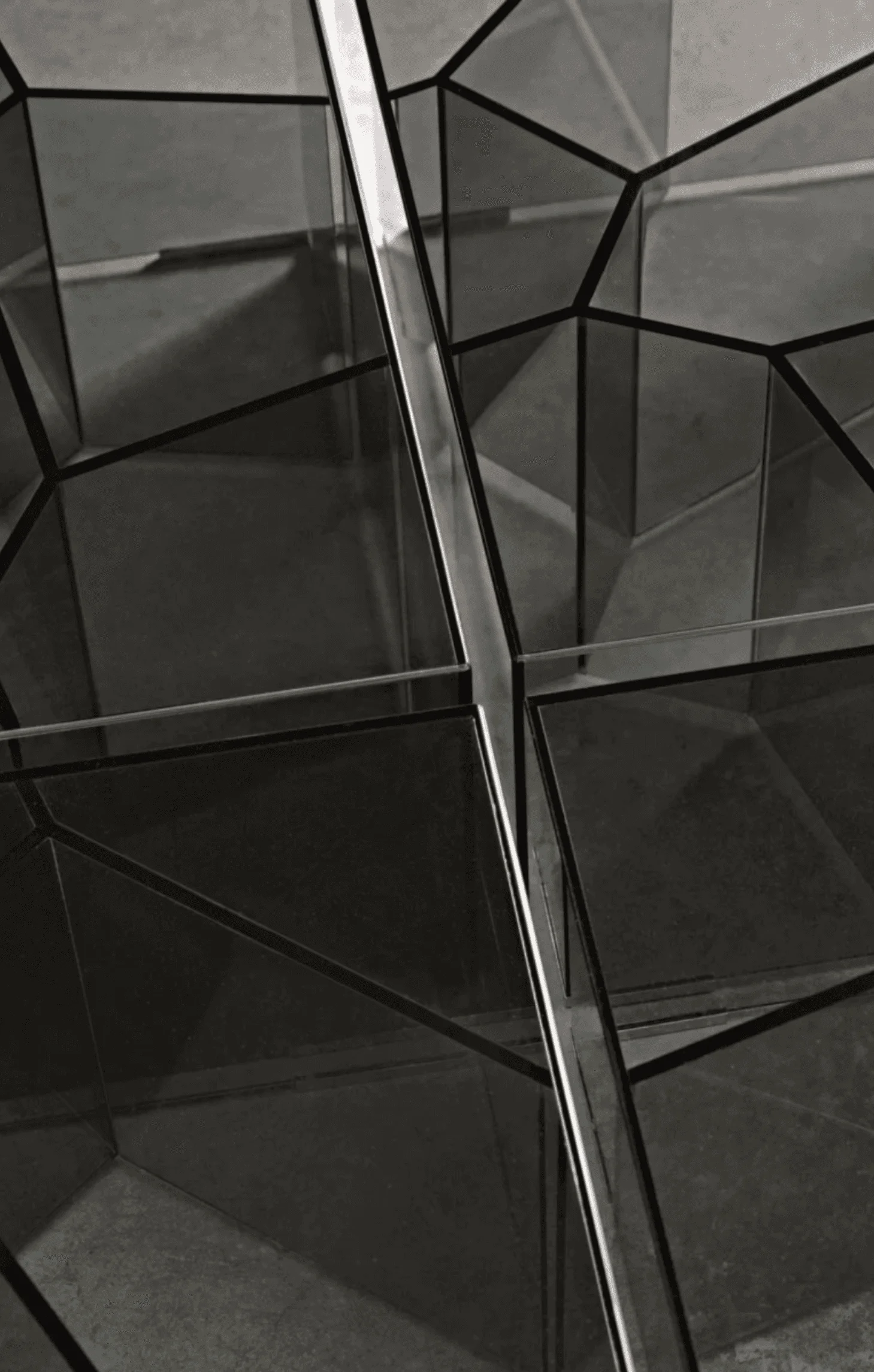 A detail of angular mirrored glass paneling with a polished steel support beam