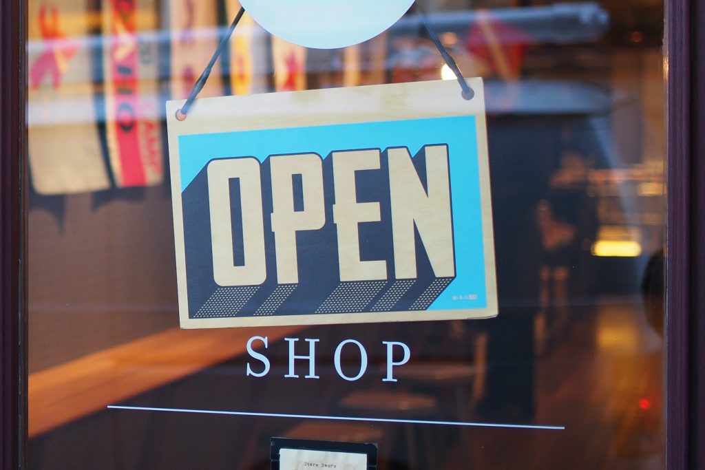 'Open' sign hanging on the glass door of a shop, about brands using Shopify Commerce Components