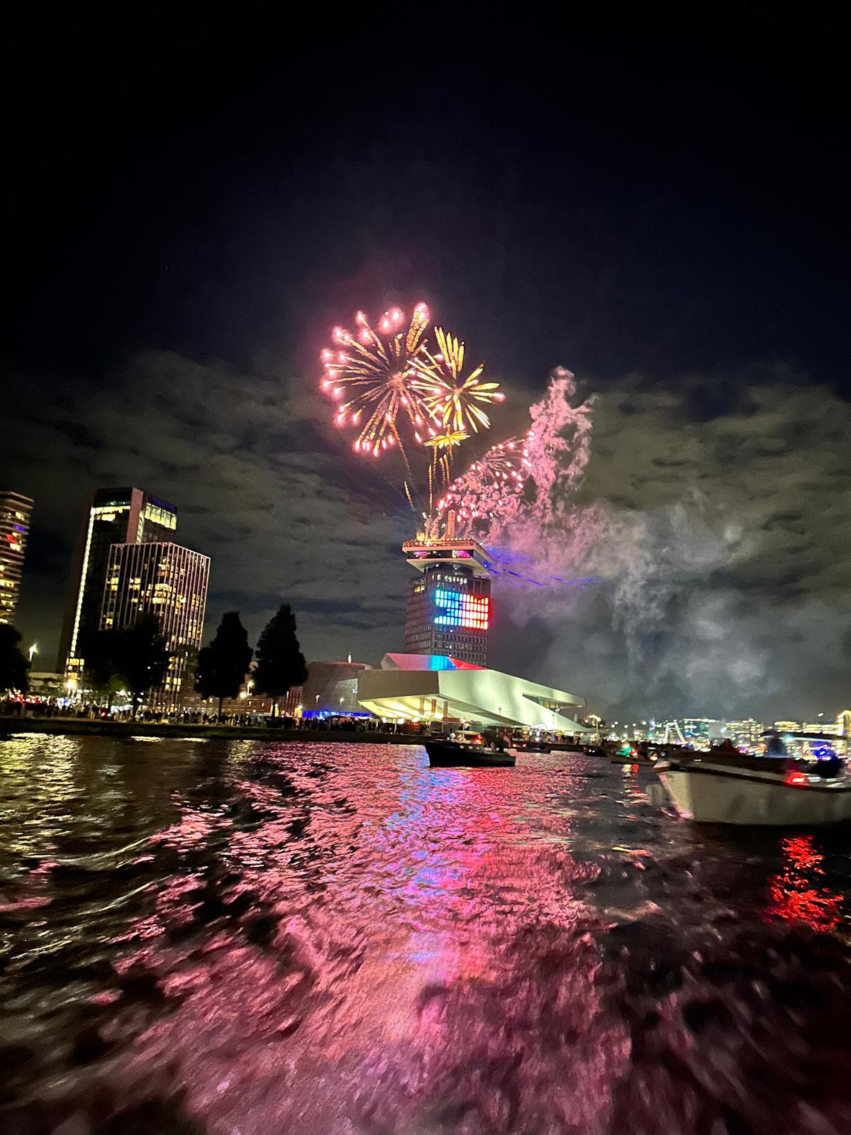 A vibrant night scene with colorful lights reflecting on water and a large projection in the sky.