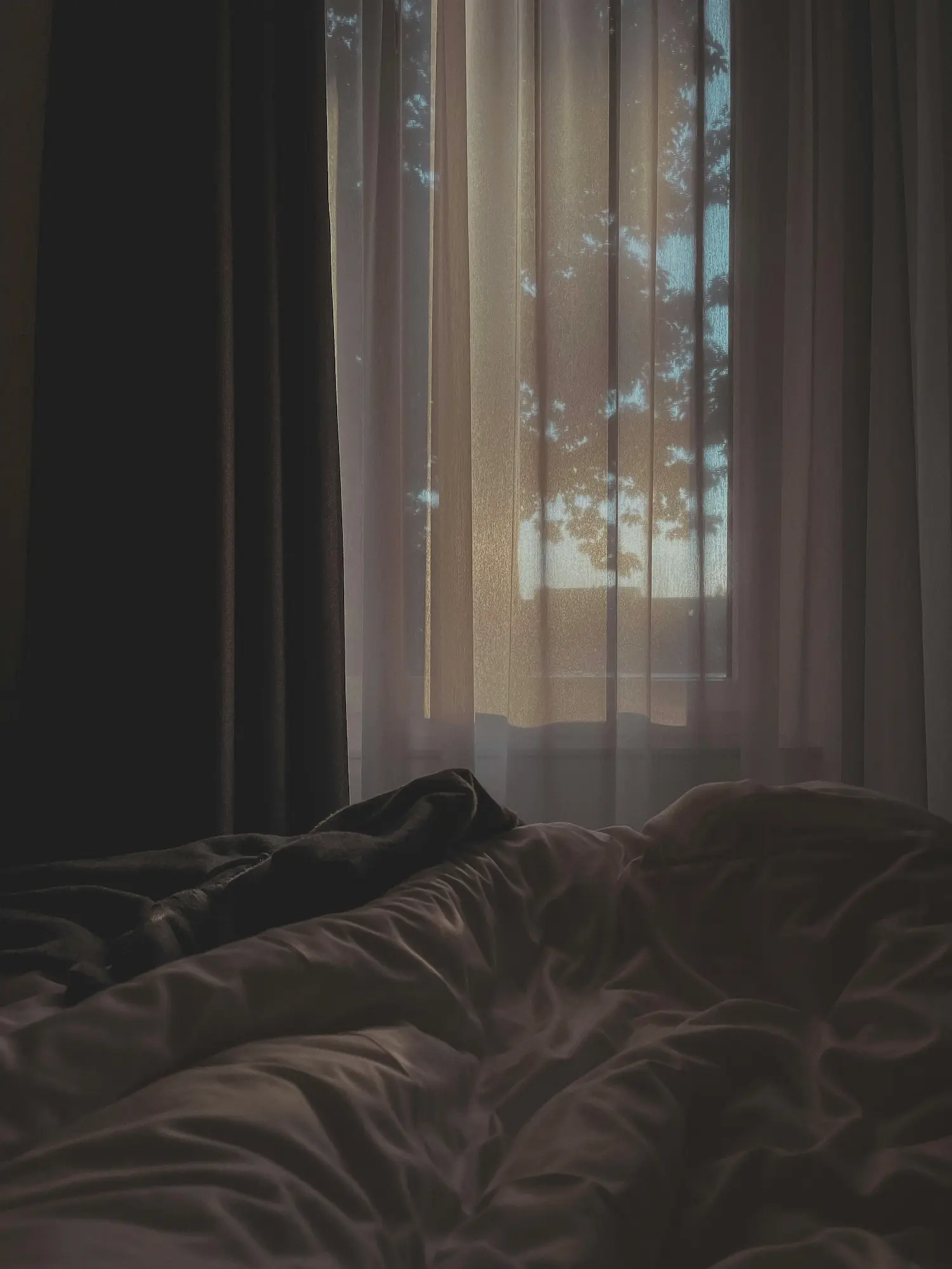 Soft morning light filters through bedroom curtains onto an unmade bed, evoking a quiet, reflective moment of intimacy. Represents the emotional depth and connection that can follow a monthly relationship check-in.