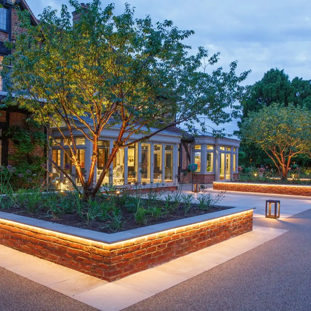 A serene outdoor space featuring landscaped areas with trees, illuminated pathways, and modern architecture at dusk.