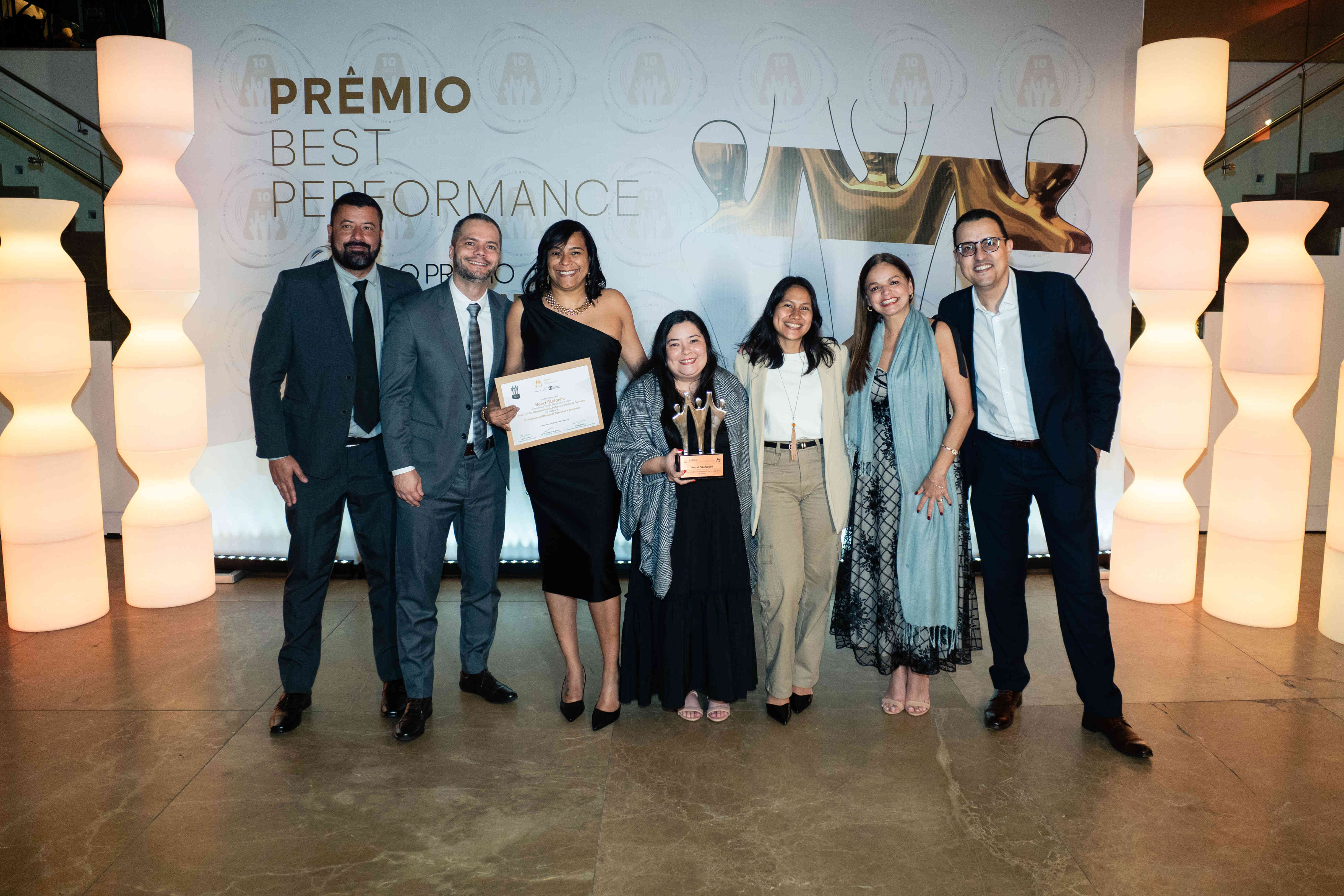 Executivos da Necxt Stefanini posando com troféu prata e certificado no palco do Prêmio Best Performance 2025