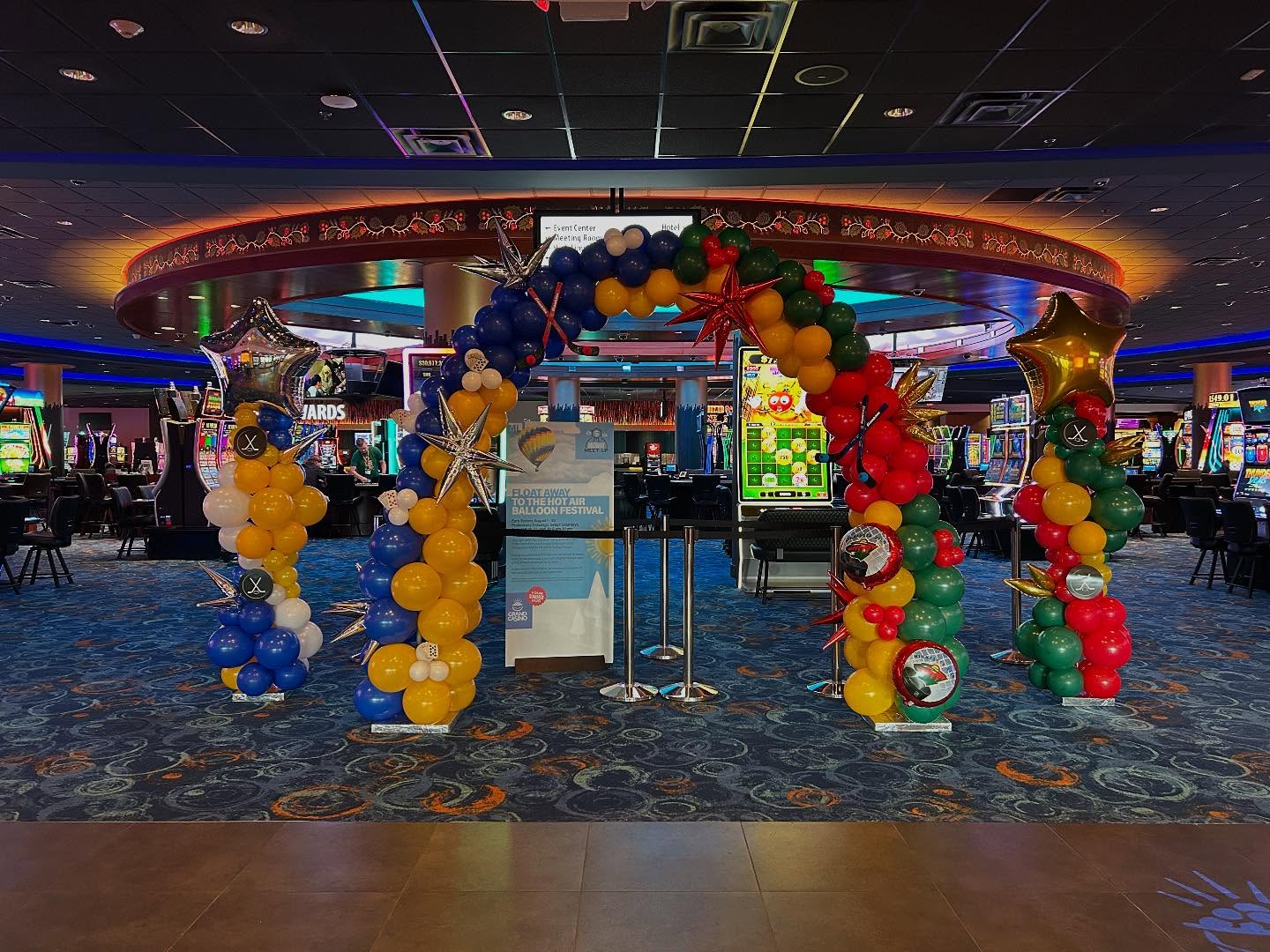Bright multicolor balloon arch featuring red, yellow, green, and blue balloons displayed at an outdoor festival by Be Bold Balloons