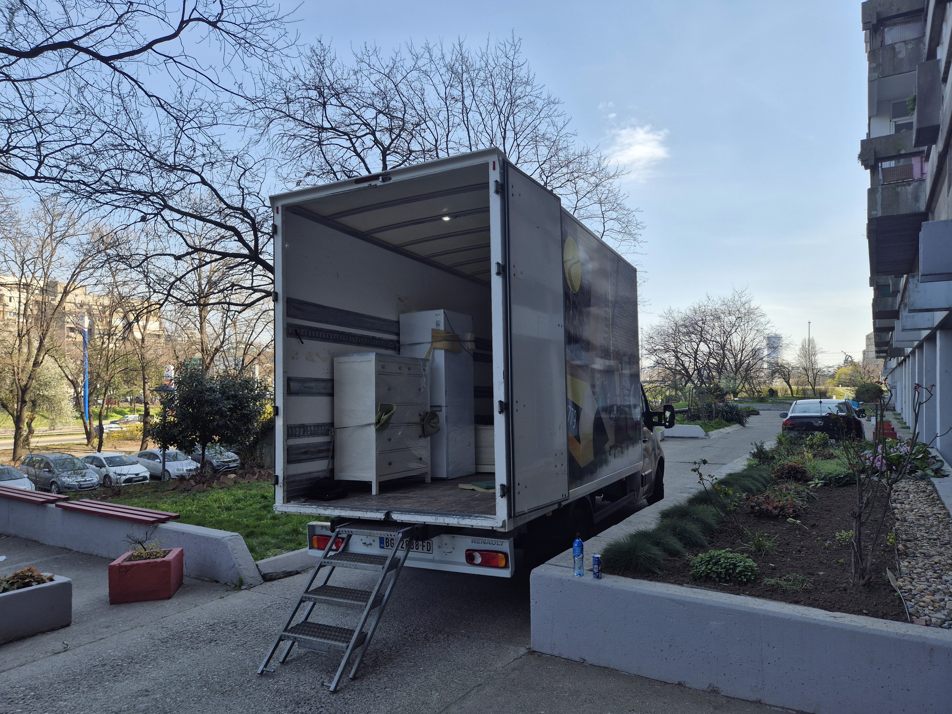 Kamion za selidbe parkiran ispred zgrade sa otvorenim tovarnim prostorom i nameštajem unutra.