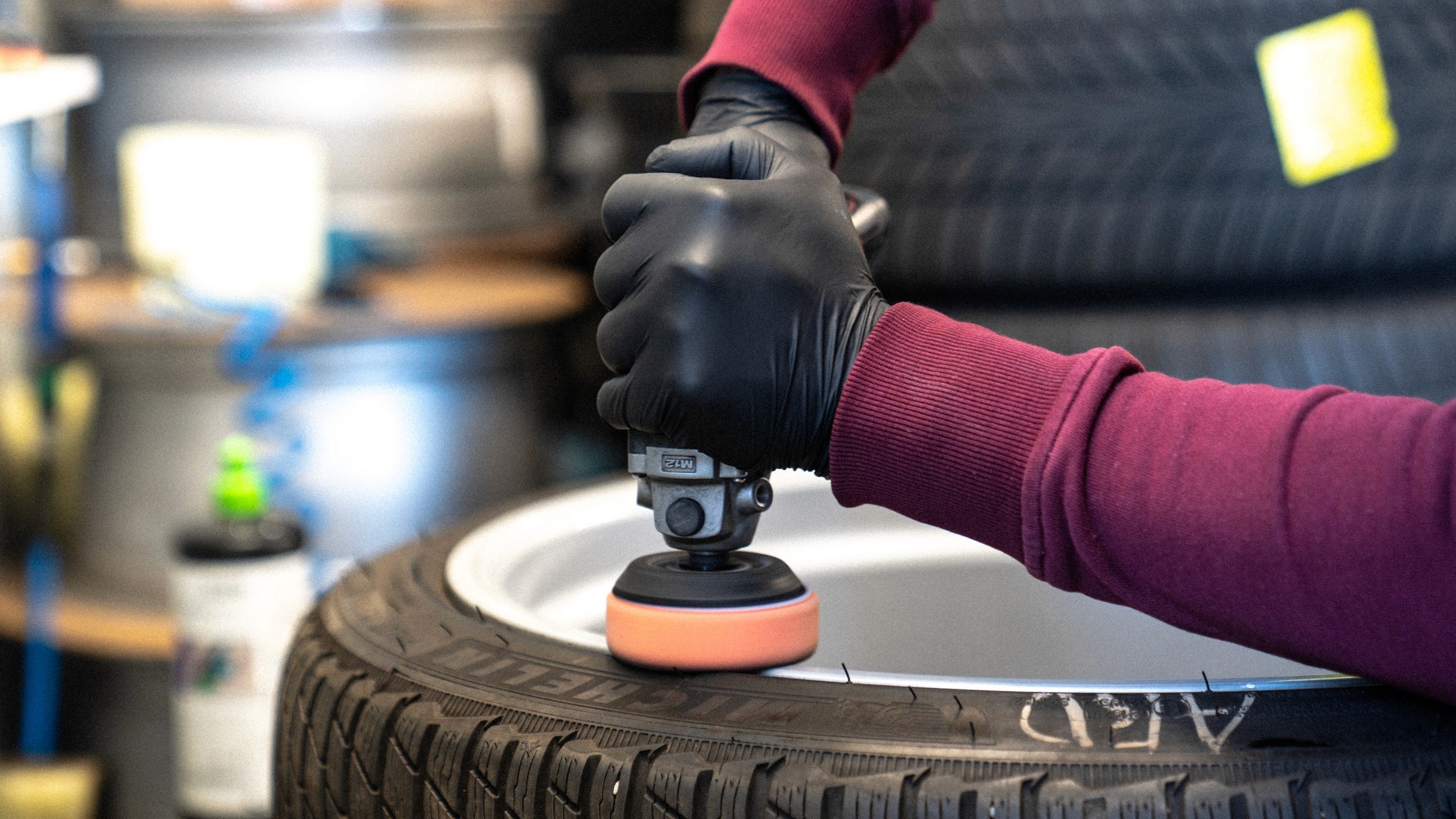 Professionelle Felgenaufbereitung: Mitarbeiter poliert eine Aluminiumfelge auf einem montierten Reifen mit Poliermaschine und Schutzhandschuhen.