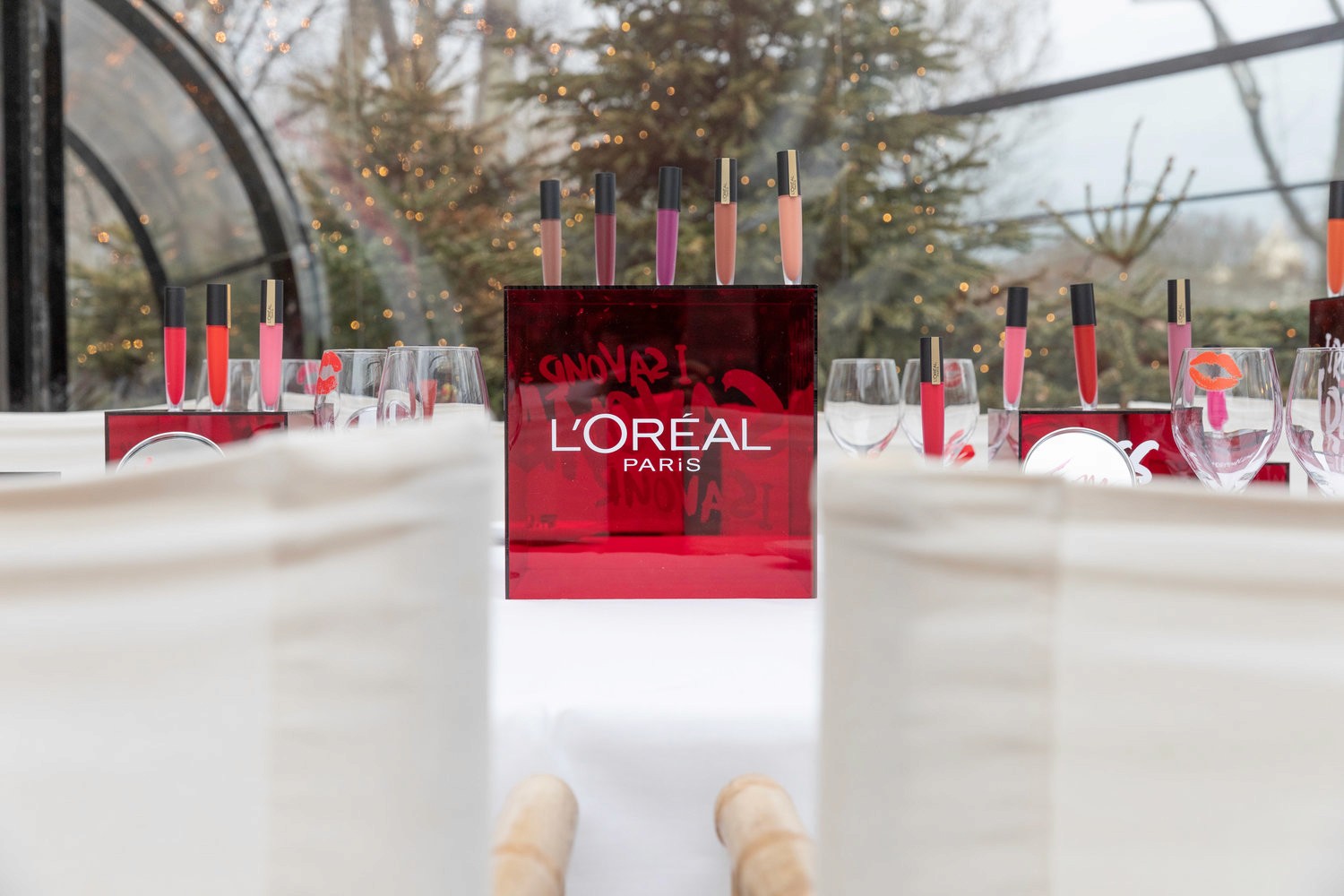  A L’Oréal Paris event setup with a red display box showcasing lip products, surrounded by glasses and festive decor.