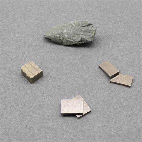 A set of diamond segments and a piece of rough stone placed on a grey surface. The segments, used for cutting hard materials like stone and concrete, are ready for industrial use.