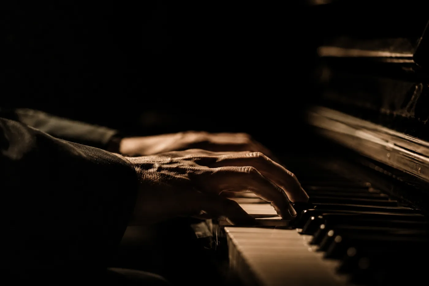 Hands playing a piano in warm, dim light
