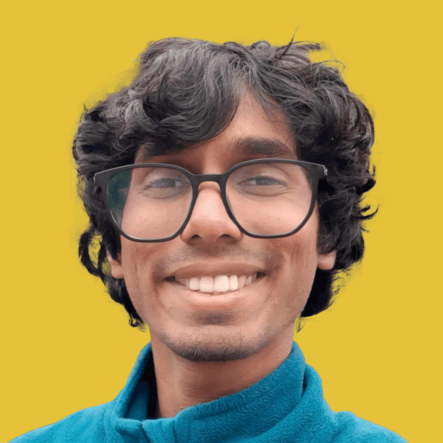 picture of team member hussain ahmed, wearing a turqoise fleece high neck sweater and glasses, smiling infront of the camera with thick fluffy black hair