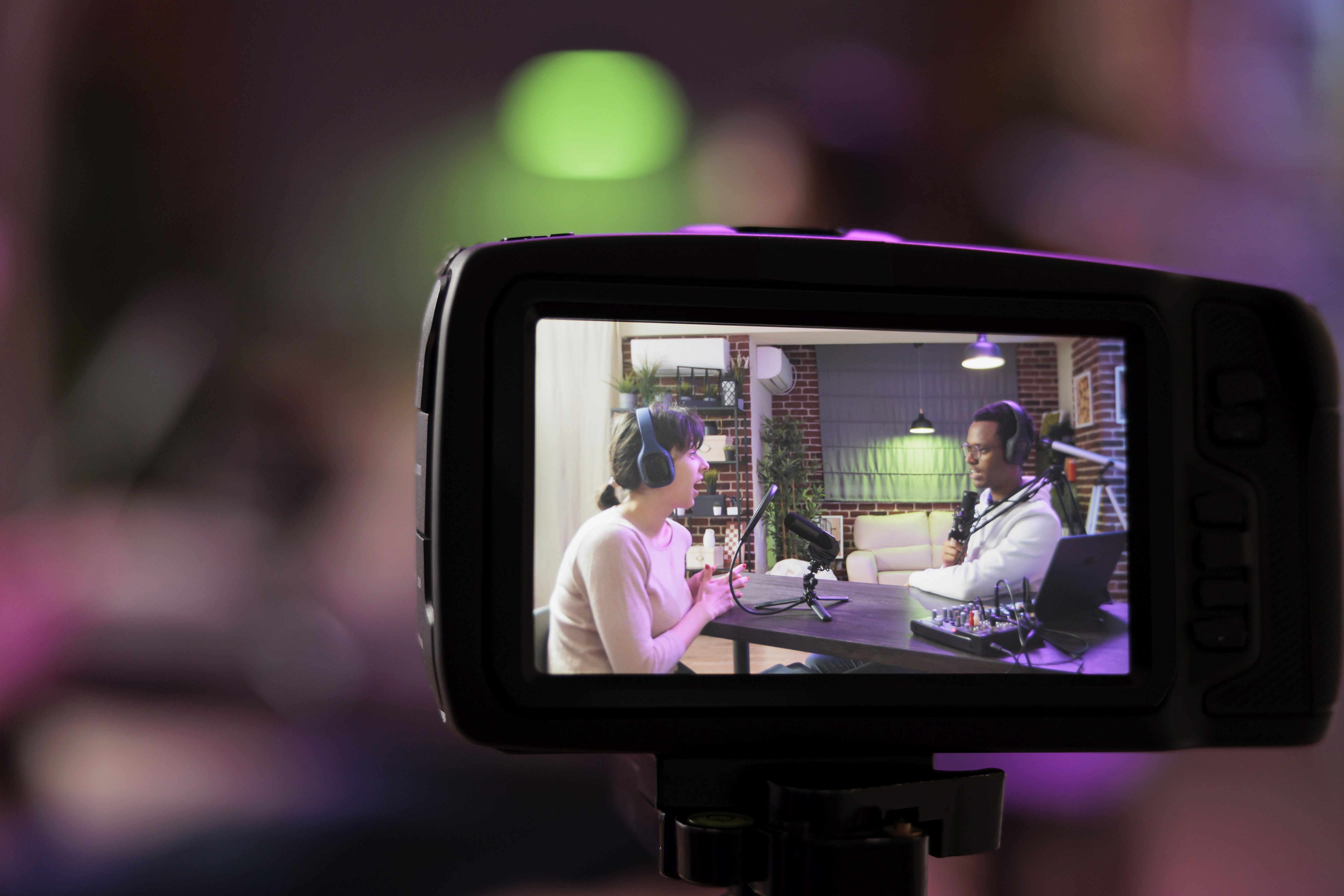 Two people recording a podcast viewed through a professional camera's LCD screen in a studio setting, representing the authentic conversational video content format that builds genuine trust with service business audiences