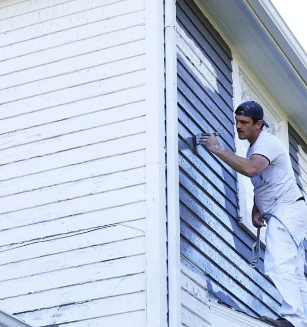 Painter applying blue paint to exterior house