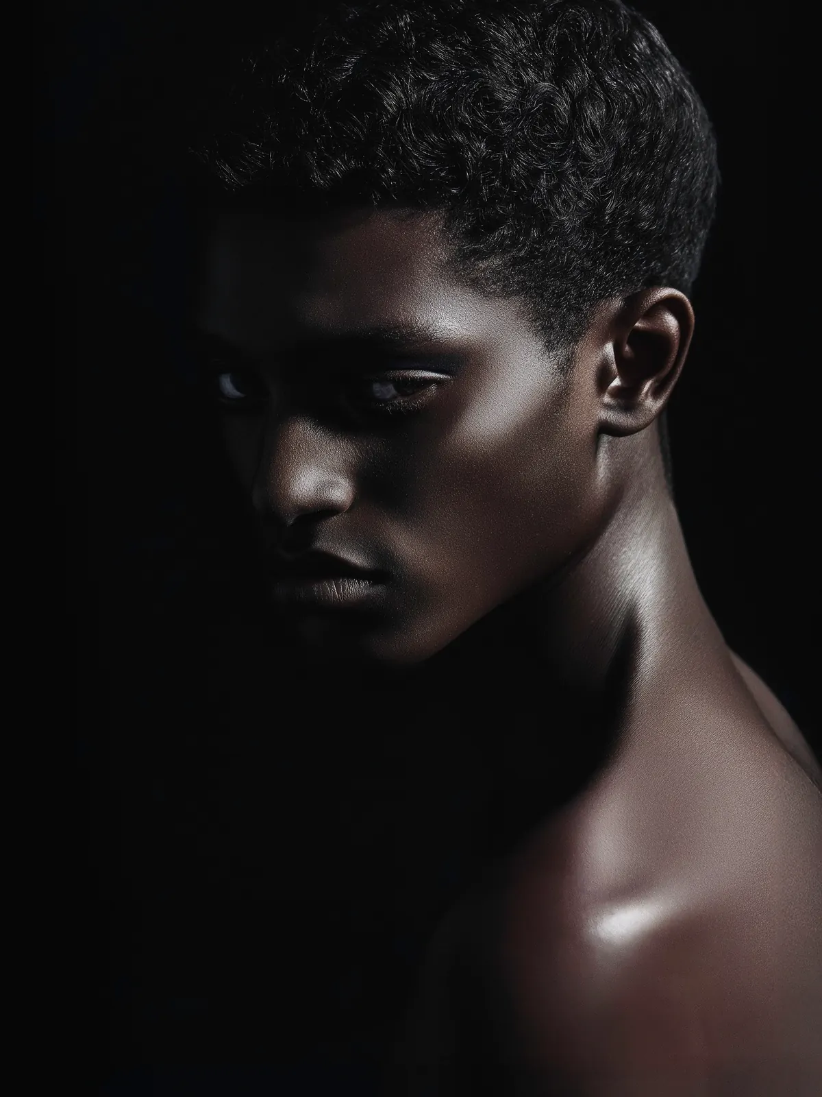 Close-up portrait with short curly hair and warm highlights against a dark background.