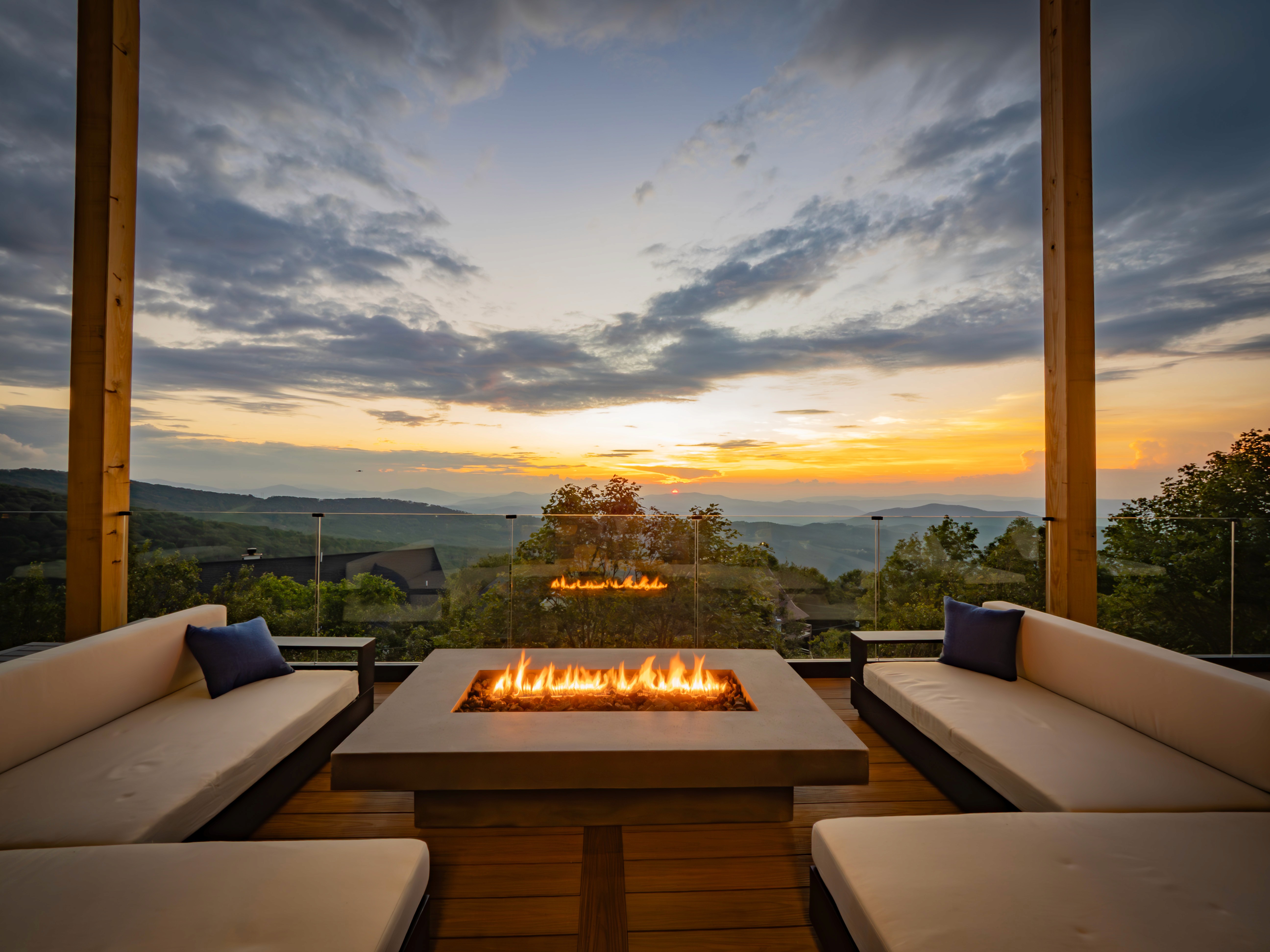 High-contrast hero shot of a modern fire pit glowing at twilight with a deep orange sun setting over the mountain range