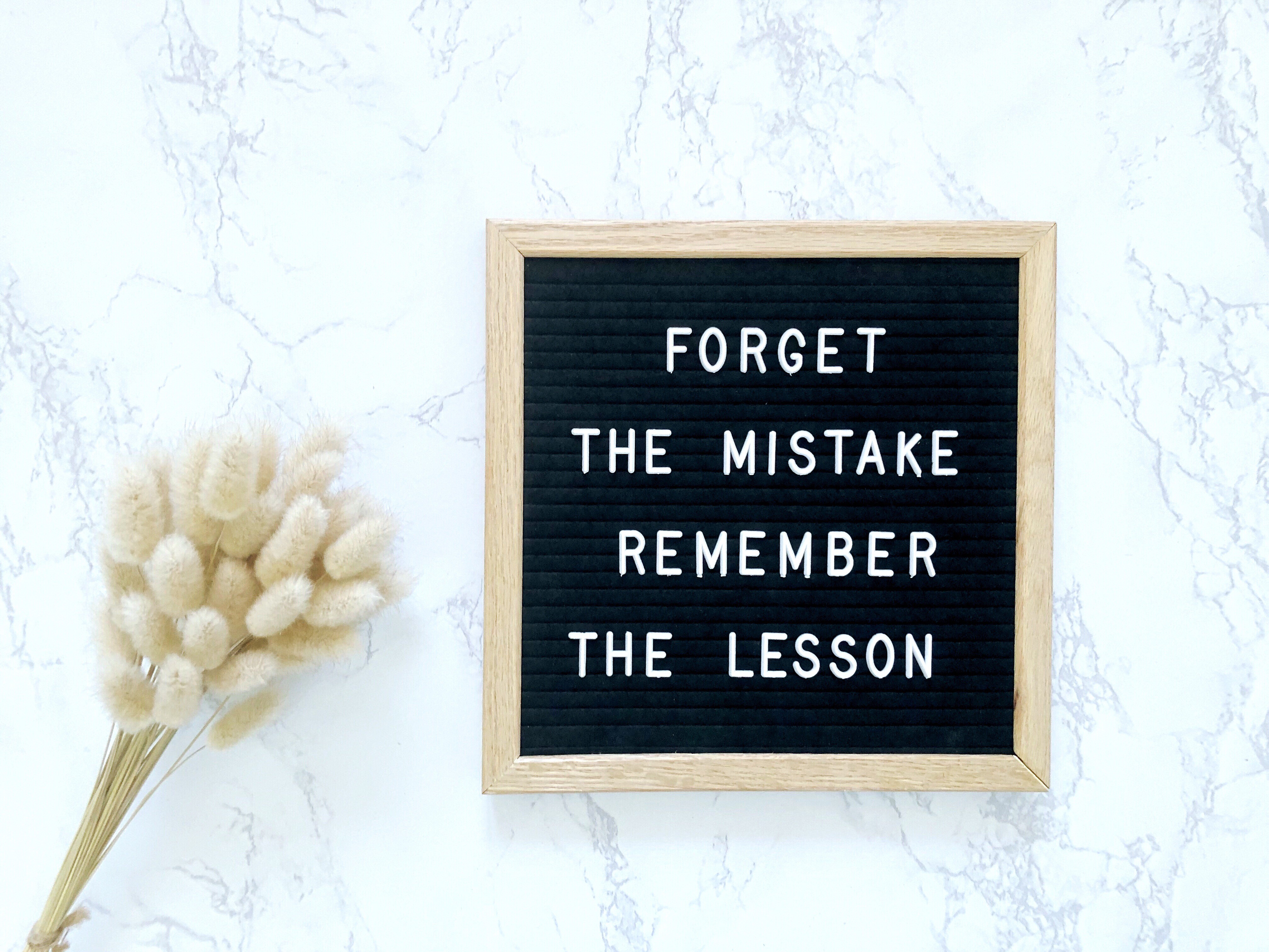 Inspirational quote board on marble background with dried flowers—text reads “Forget the mistake, remember the lesson,” symbolizing personal growth and positive mindset.