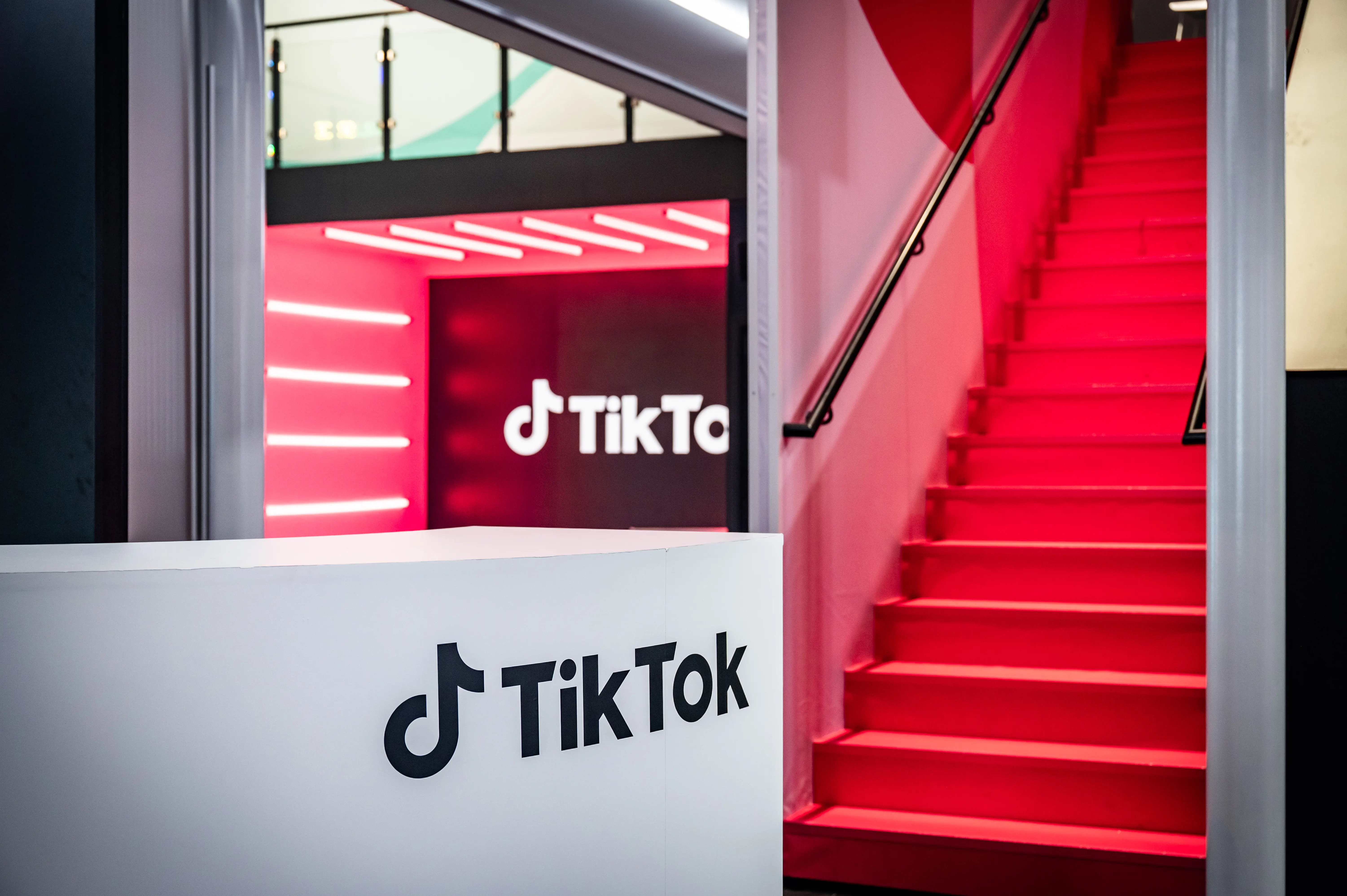 White reception desk with TikTok logo in front of the red staircase and glowing studio entrance.
