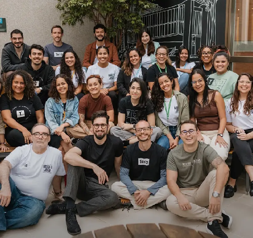 Um grande grupo de pessoas da Tera posando juntas ao ar livre, sorrindo e sentadas em um ambiente casual.