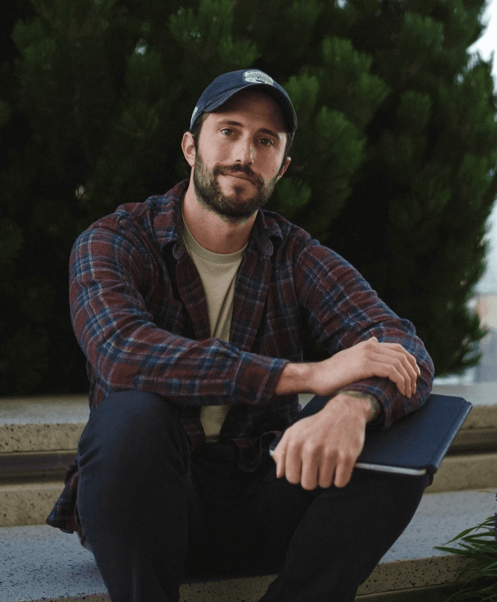 Person wearing a blue puffer jacket and red backpack standing in front of a light blue building on a city street.