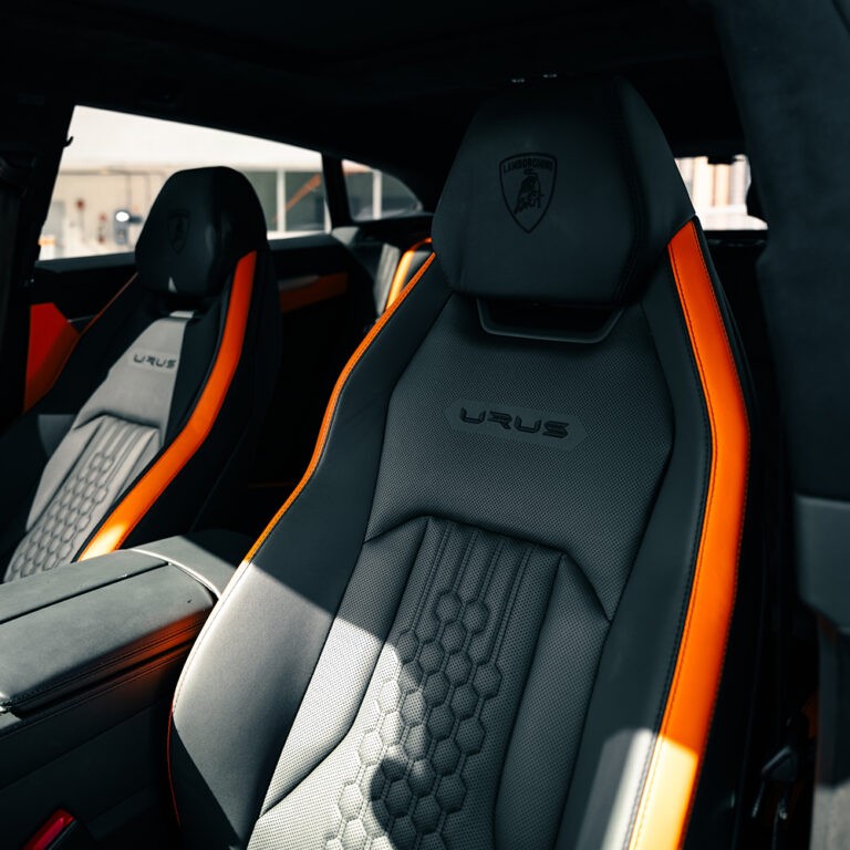 Front seats of blue Lamborghini Urus S, orange leather trim, premium car rental interior.