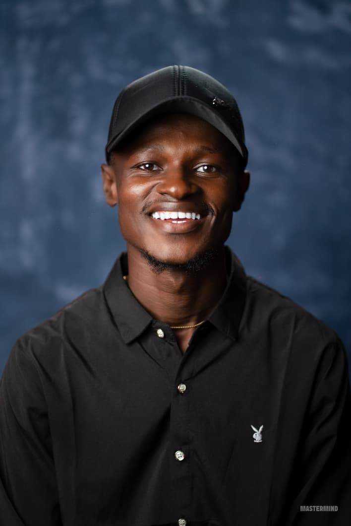 A person wearing headphones sits at a desk with a large curved monitor displaying graphic design software, surrounded by a laptop, smartphone, and potted plant, creating a modern workspace setup.