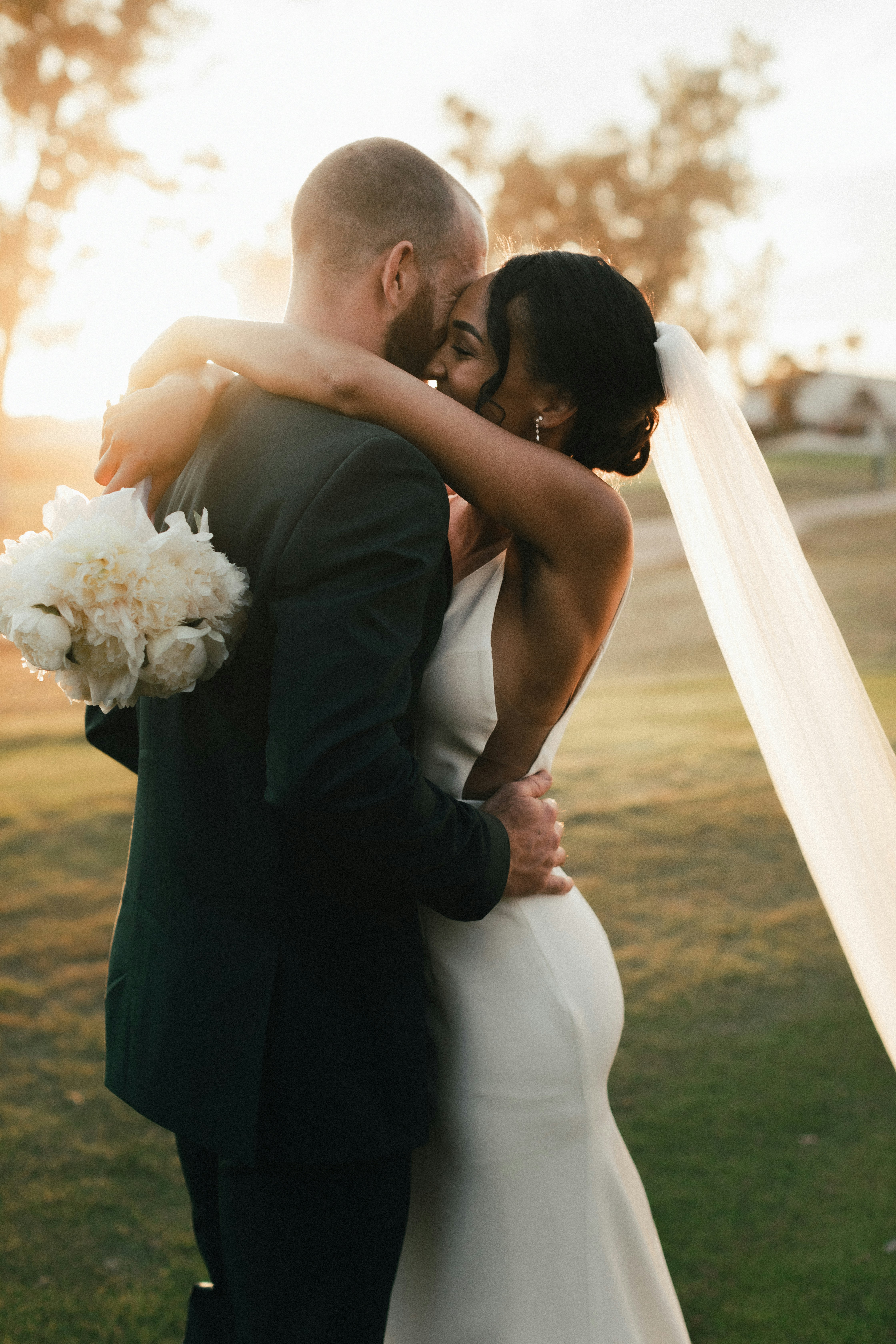 A couple in wedding attire walks hand in hand across a sunlit field.