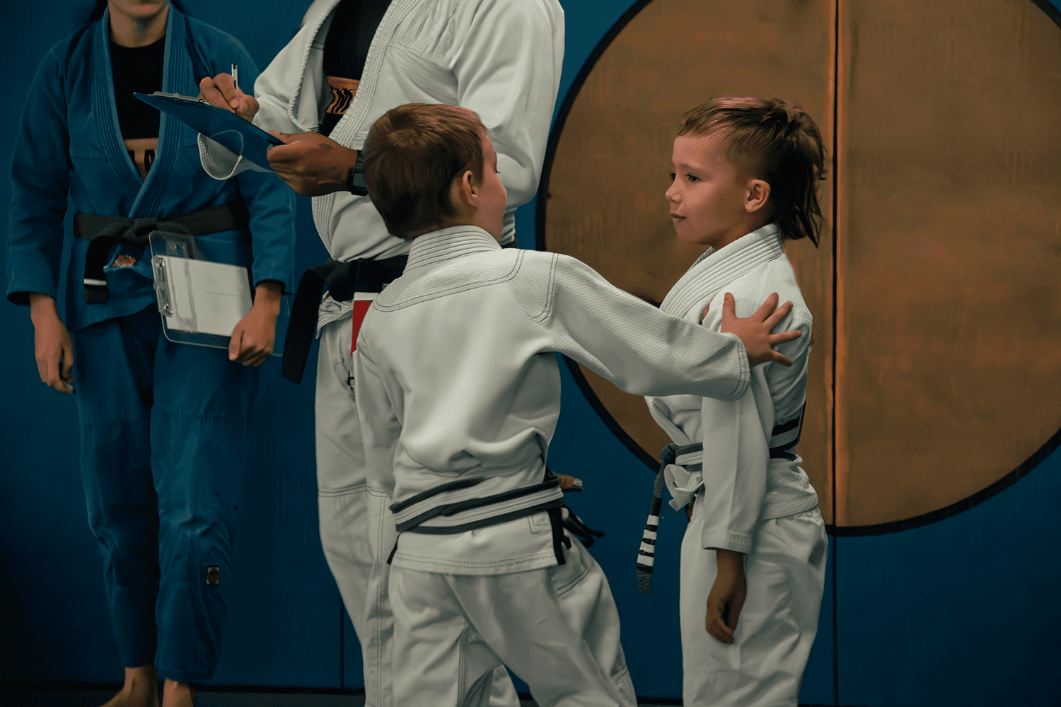 Two young students practicing Jiu Jitsu with an instructor observing