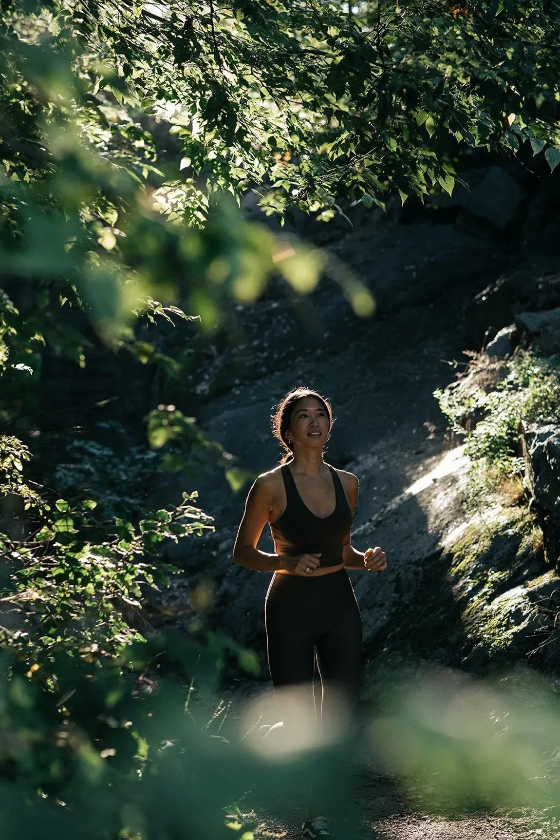 一位穿著運動服的女士在林蔭小道上慢跑,在翠綠的樹葉和陽光的穿透下練習正念和修身連結。