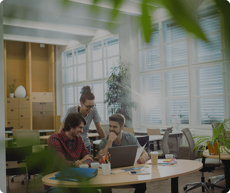 Group of colleagues collaborating and smiling around a laptop in a bright modern office.
