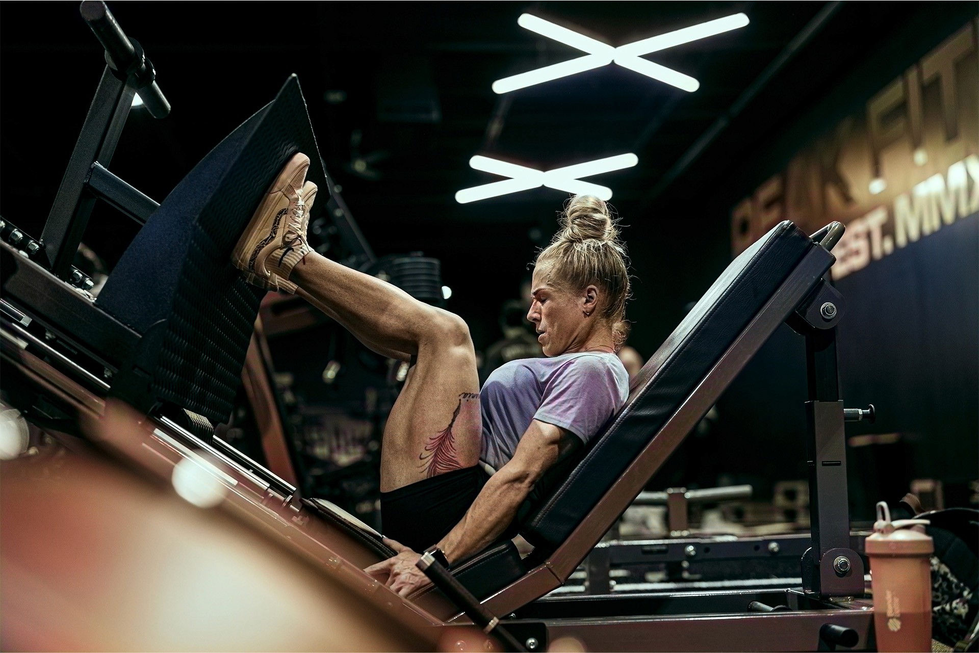 Eine athletische blonde Frau an einer Beinpresse, mit angestrengtem Blick.