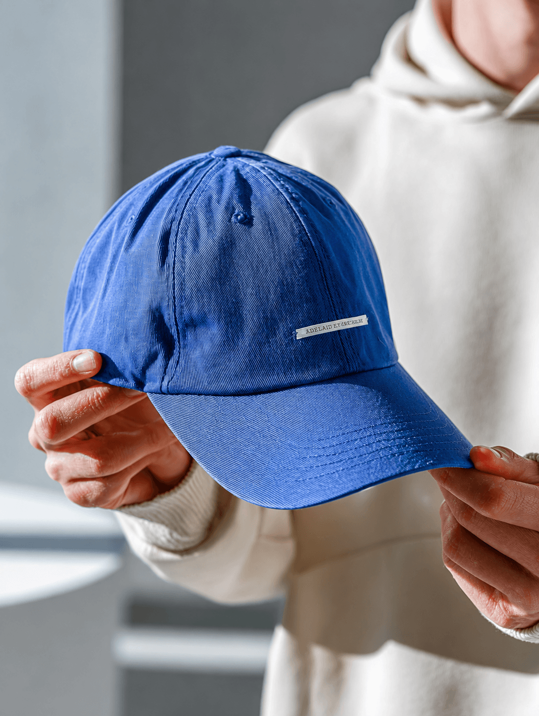 Person holding a bright blue baseball cap in a soft natural light studio setting