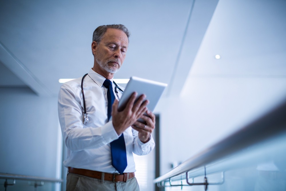 Male professional in a white coat reviewing notes on a tablet, representing digital safety checks and evidence capture.