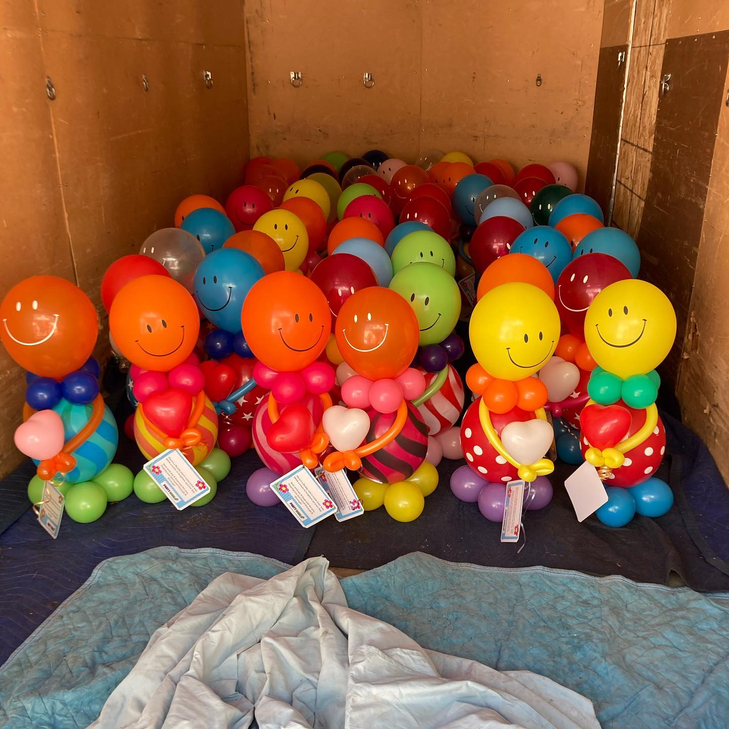 Colorful balloon figures with smiling faces, dressed in various vibrant patterns and stripes, are neatly arranged inside a large cardboard box.