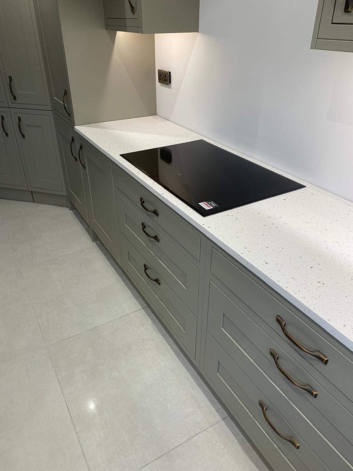 Sage green shaker kitchen cabinets with a quartz worktop and modern induction hob, installed by PPM Builders in Northampton. Elegant brass handles and under-cabinet lighting enhance the stylish design.