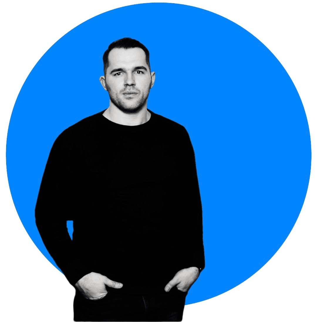 Tim Tesluck stands in a black shirt against a large blue circular background.