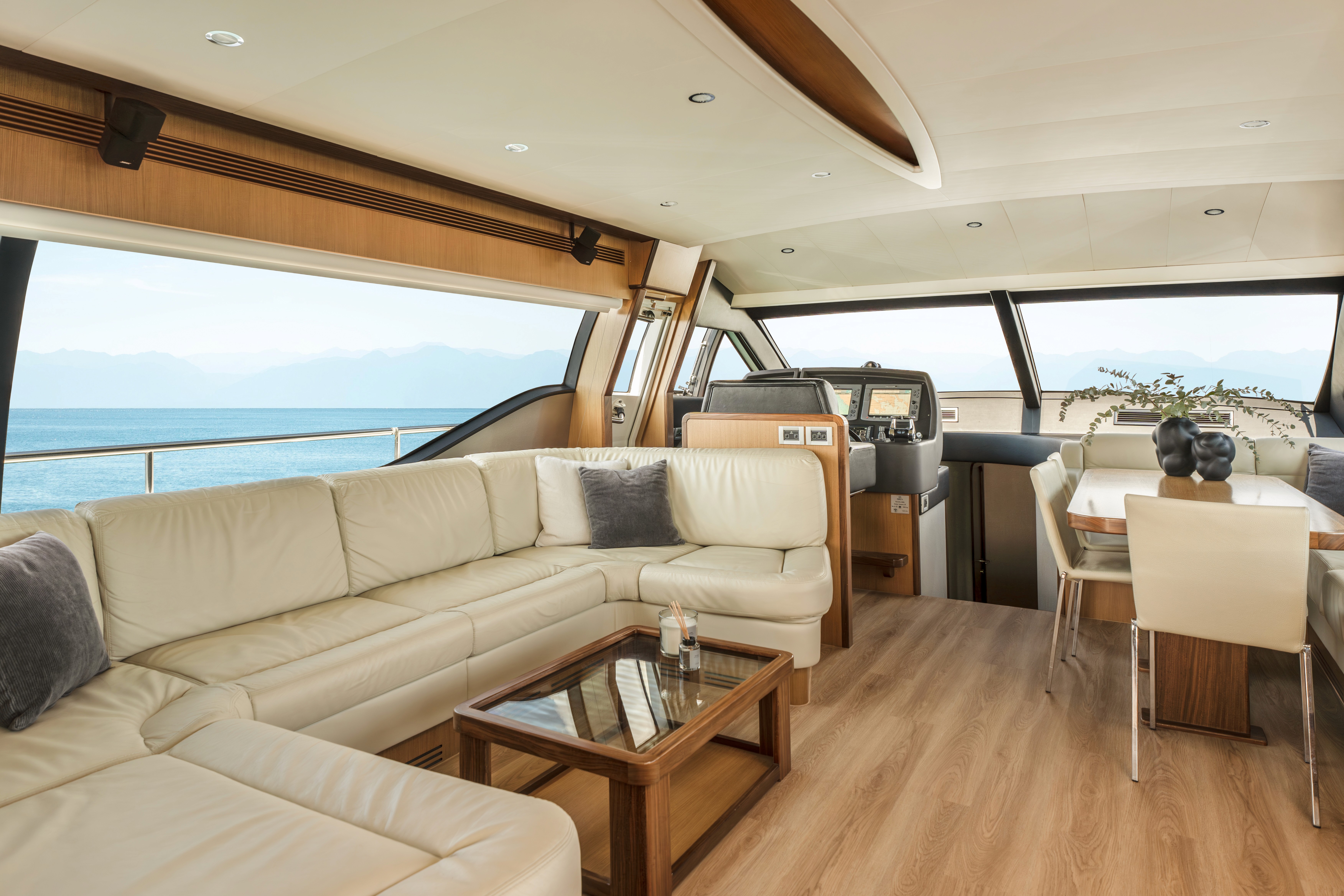 Luxurious main salon of Ferretti 63 yacht featuring cream leather U-shaped seating, wood coffee table, and panoramic windows overlooking calm blue waters.