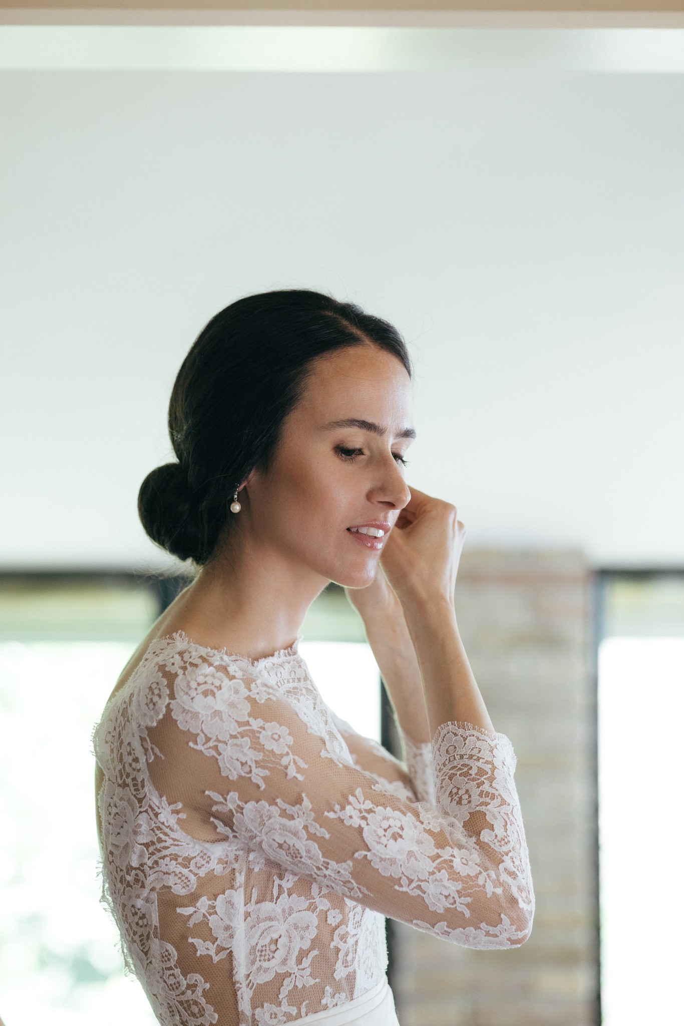 Sposa in pizzo osserva i dettagli dei preparativi matrimoniali, illuminata dalla luce naturale della finestra