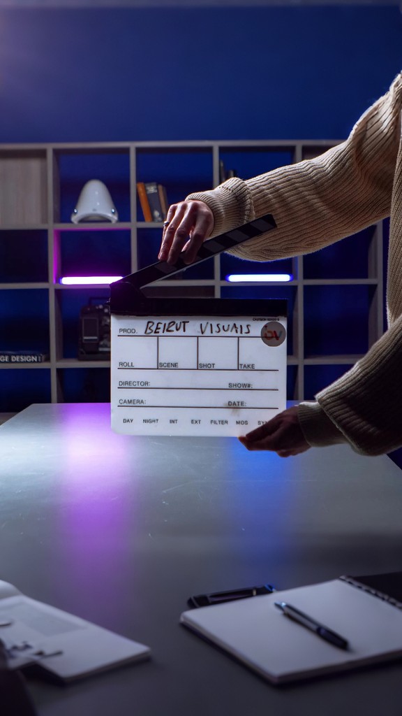Close-up portrait of a person wearing a gray insulated hooded jacket with the hood up, showing their face framed by the hood against a light background.