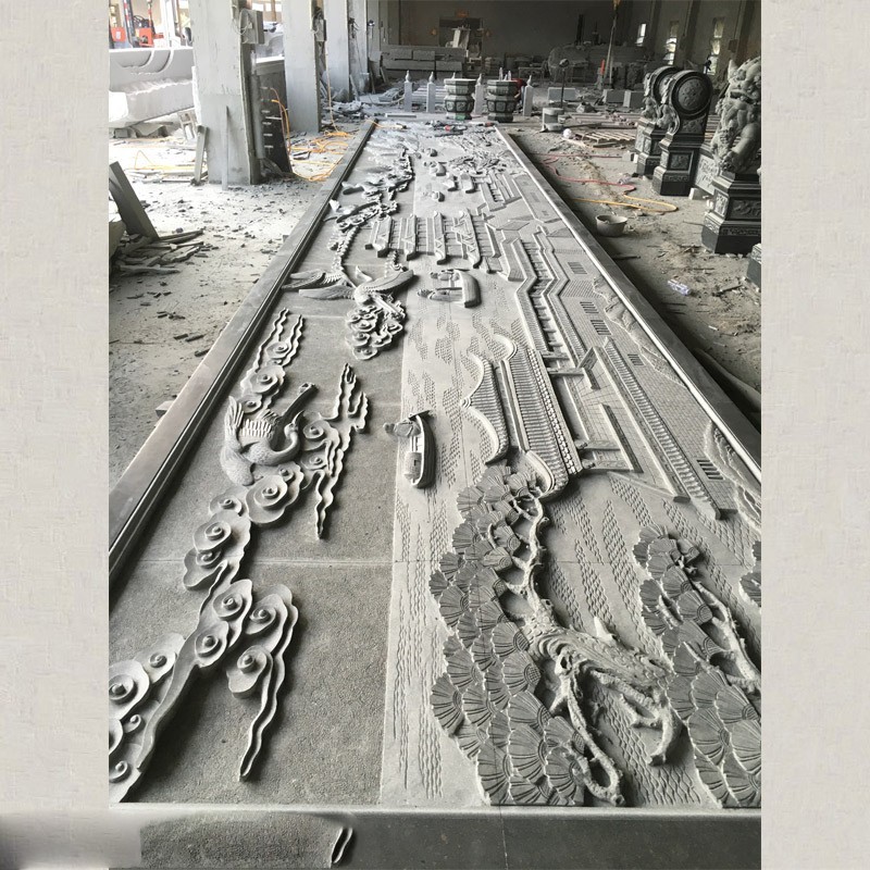 An intricately carved stone relief panel in a workshop, showcasing traditional Chinese landscape and architectural elements.