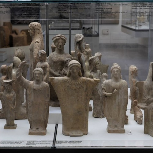 博物館のガラスケースの中に陳列された、様々なポーズを取った古代のテラコッタ人形の展示。