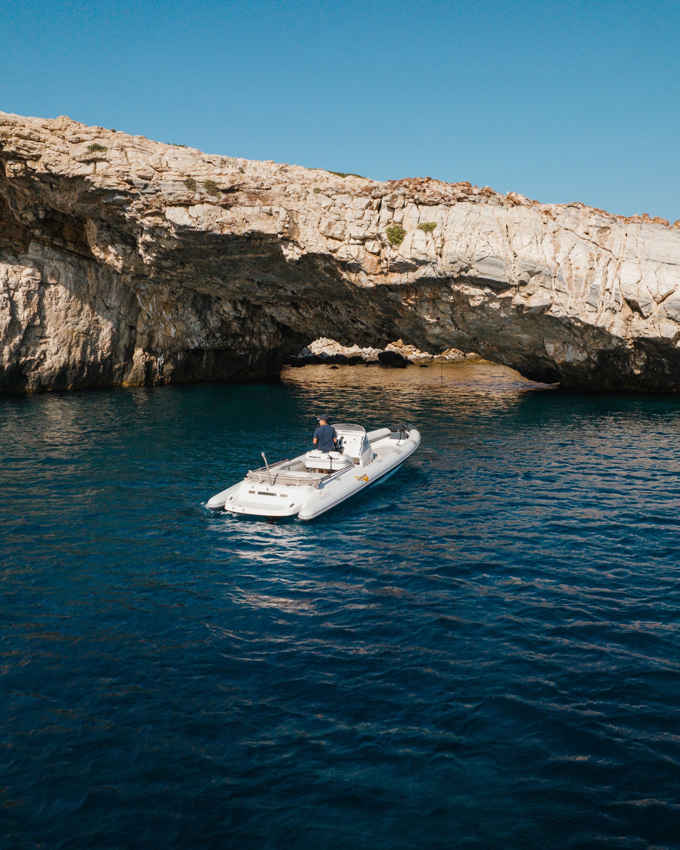 White Airship 30 Aether yacht anchored in crystal-clear turquoise waters near dramatic limestone cliffs with passengers relaxing on deck.