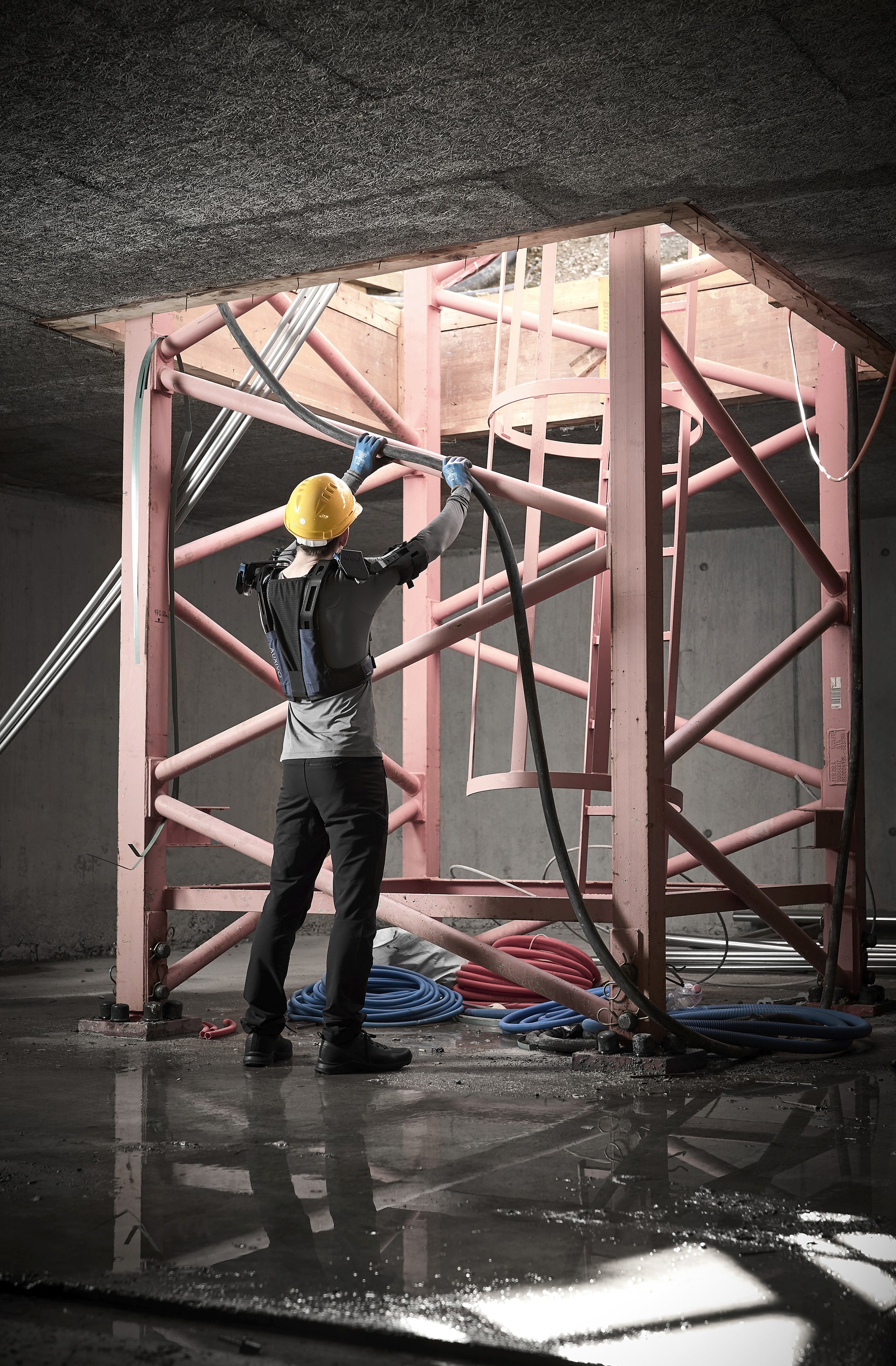 Construction worker performing a task with arms raised while wearing the DeltaSuit exoskeleton, designed to reduce shoulder fatigue and support work at heights on the job site.