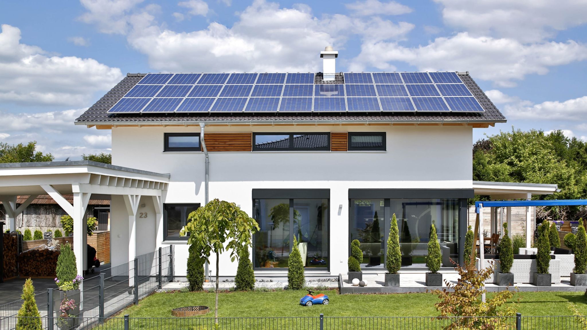 Modernes Einfamilienhaus mit Solaranlage auf dem Dach, Carport und gepflegtem Garten.