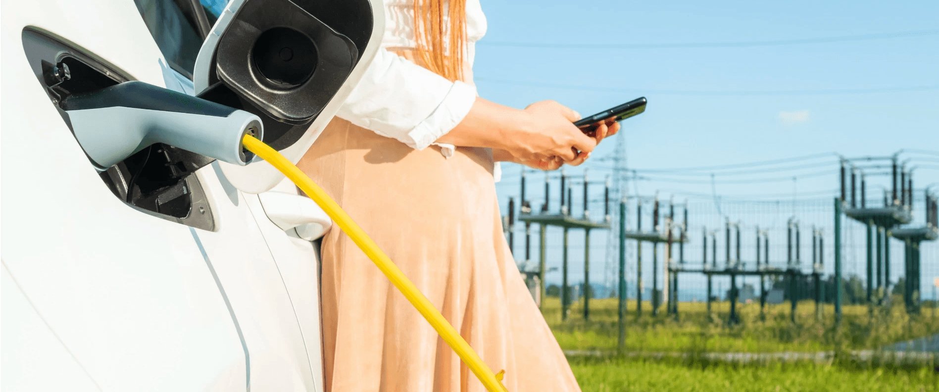 Person standing next to an electric vehicle while charging, checking a mobile device, symbolizing the availability of the conference program for the electromobility event now accessible online